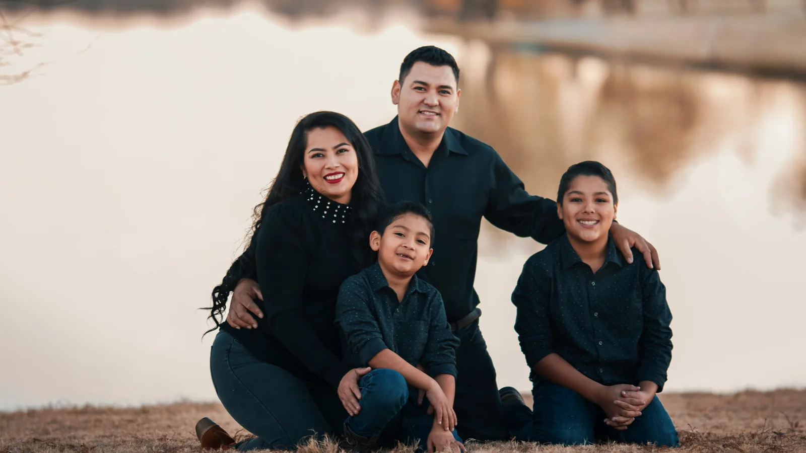 A smiling family of four outdoors, by a lake.